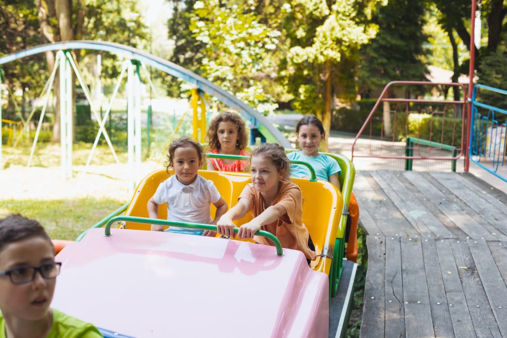 The happy little kids ride on a roller coaster in the amusement park on sunny day