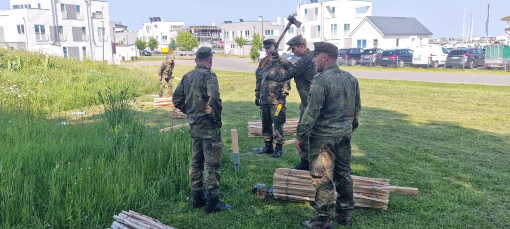 ↑ Viele freiwillige Helfer der Marine unterstützen den Aufbau des neuen Artenschutzpfades im OstseeResort Olpenitz. Vor Ort helfen sie beim Setzen des Staketenzauns, der den Startpunkt des Pfades künftig einrahmen soll.
